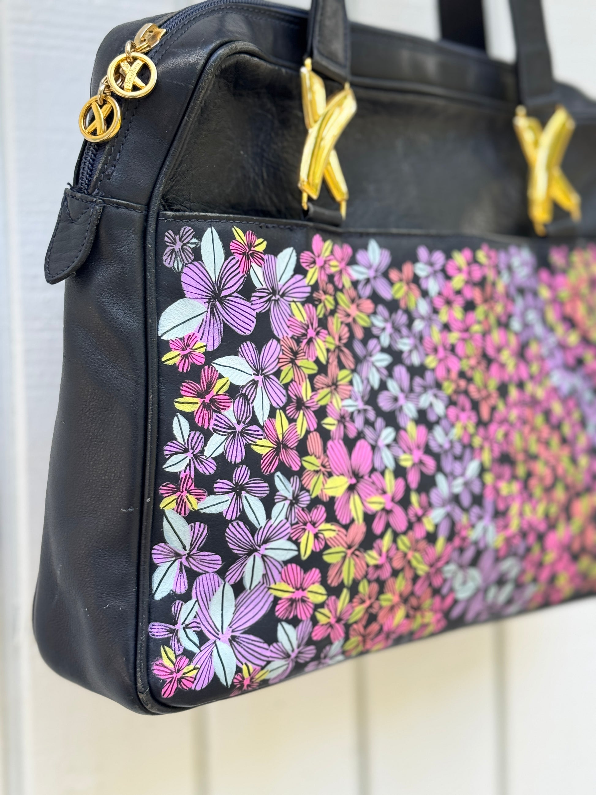 Navy leather bag by Paloma Picasso. This bag is from the 1990s. I painted multicolored flowers on it using Posca paint pens. The purse has shoulder straps with the iconic ‘X’ gold tone metal hardware linking them to the purse.

Corner view there is some light wear on the corner as it’s a vintage purse.