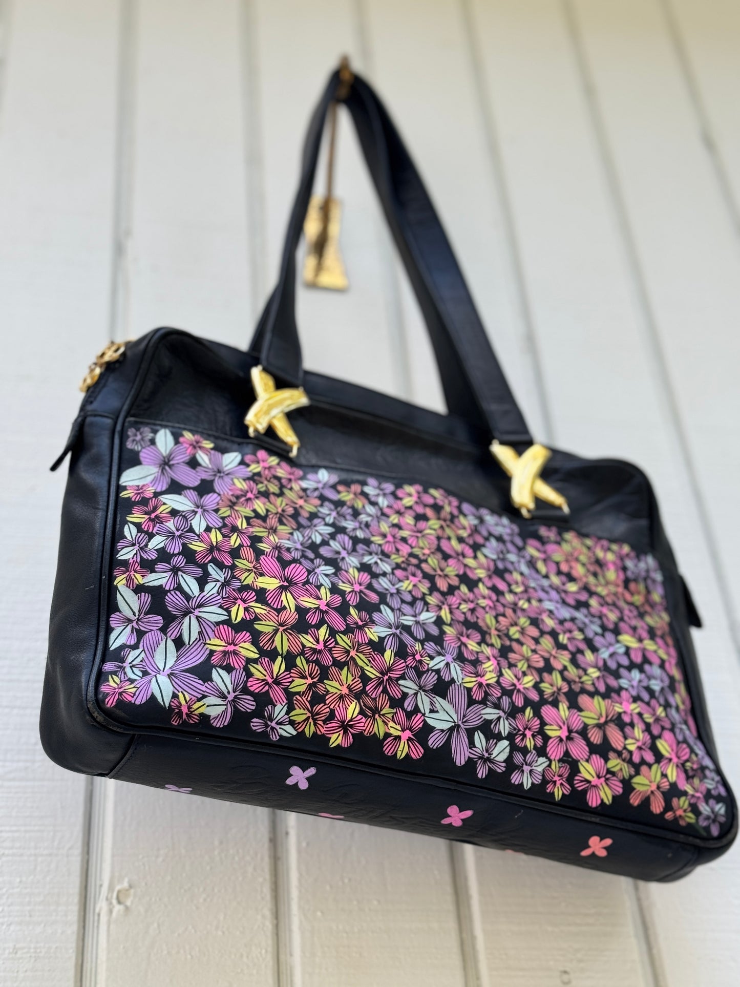 Navy leather bag by Paloma Picasso. This bag is from the 1990s. I painted multicolored flowers on it using Posca paint pens. The purse has shoulder straps with the iconic ‘X’ gold tone metal hardware linking them to the purse.

Shoot of the bottom of the bag where there are a few more flowers painted on. 