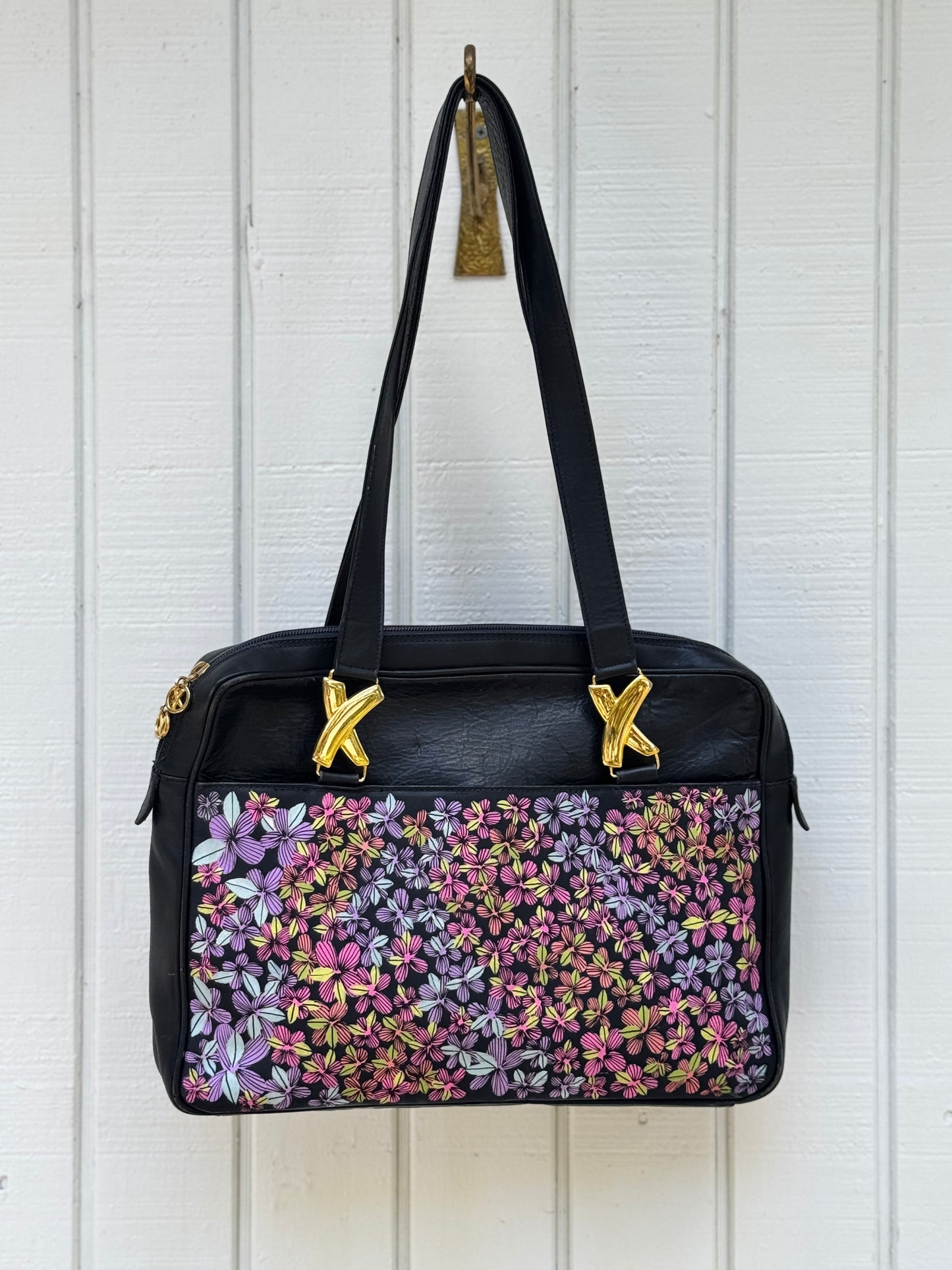 Navy leather bag by Paloma Picasso. This bag is from the 1990s. I painted multicolored flowers on it using Posca paint pens. The purse has shoulder straps with the iconic ‘X’ gold tone metal hardware linking them to the purse.